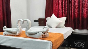 A hotel room with a bed, red curtains, a white pillow, and two towels shaped like swans.
