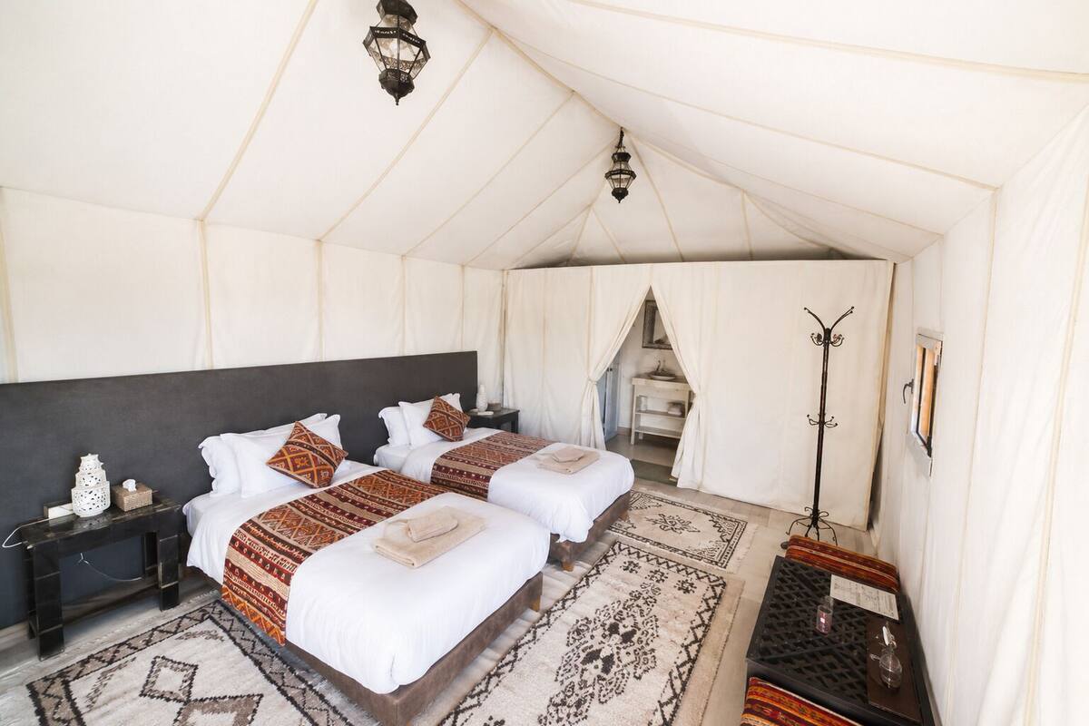Una habitación con carpa, dos camas, una mesita de noche, una lámpara y un espejo.