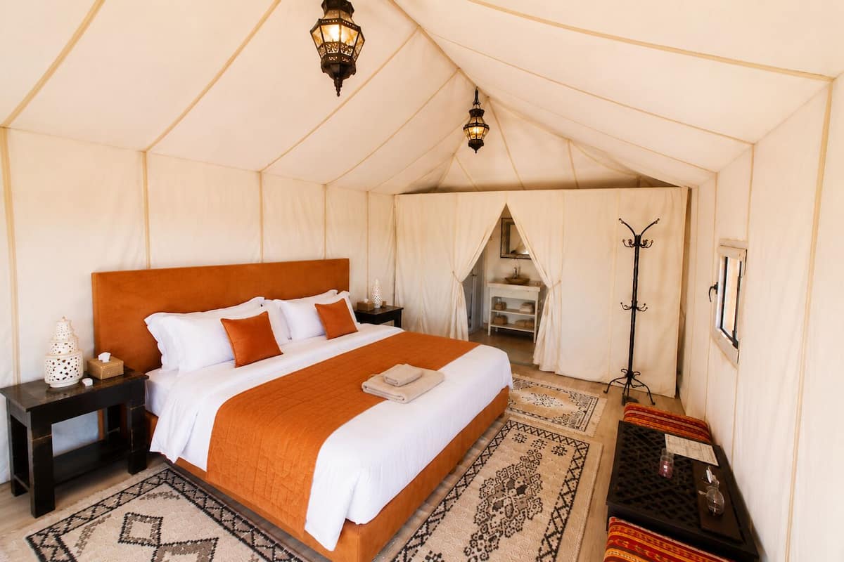 Una habitación con carpa que incluye una cama, mesitas de noche, una lámpara y un perchero.