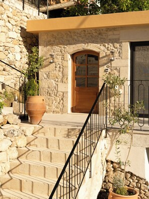 A stone building with a wooden door, a large terracotta pot, and a metal staircase. - Sterna Slow Living Home (Rethymno)