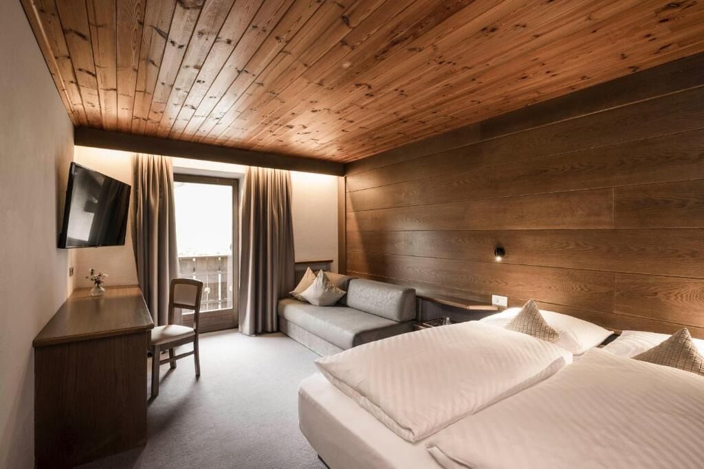 Ein Hotelzimmer mit Holzboden, einem Bett, einer Couch, einem Schreibtisch und einem Fernseher.
