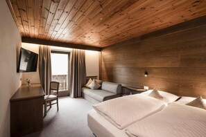 Habitación de hotel con techo de madera, cama, sofá, escritorio y televisor.