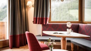 Una habitación acogedora con una mesa de madera, una silla roja, un banco y una ventana con cortinas.