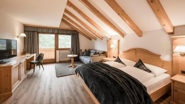 Un dormitorio con cama, vigas de madera, escritorio, silla, televisor y ventana.