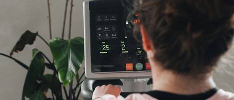 A person using a stationary bike with a digital display, a potted plant, and a wall in the background.