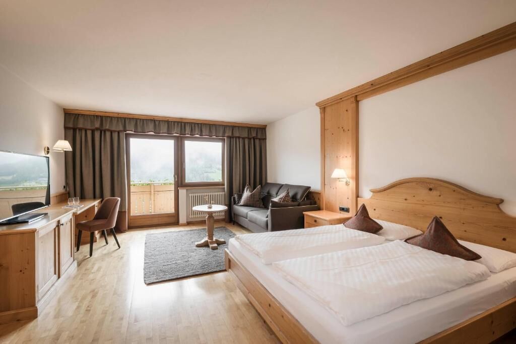 A hotel room with a bed, a desk, a chair, a sofa, and a view of the outdoors.