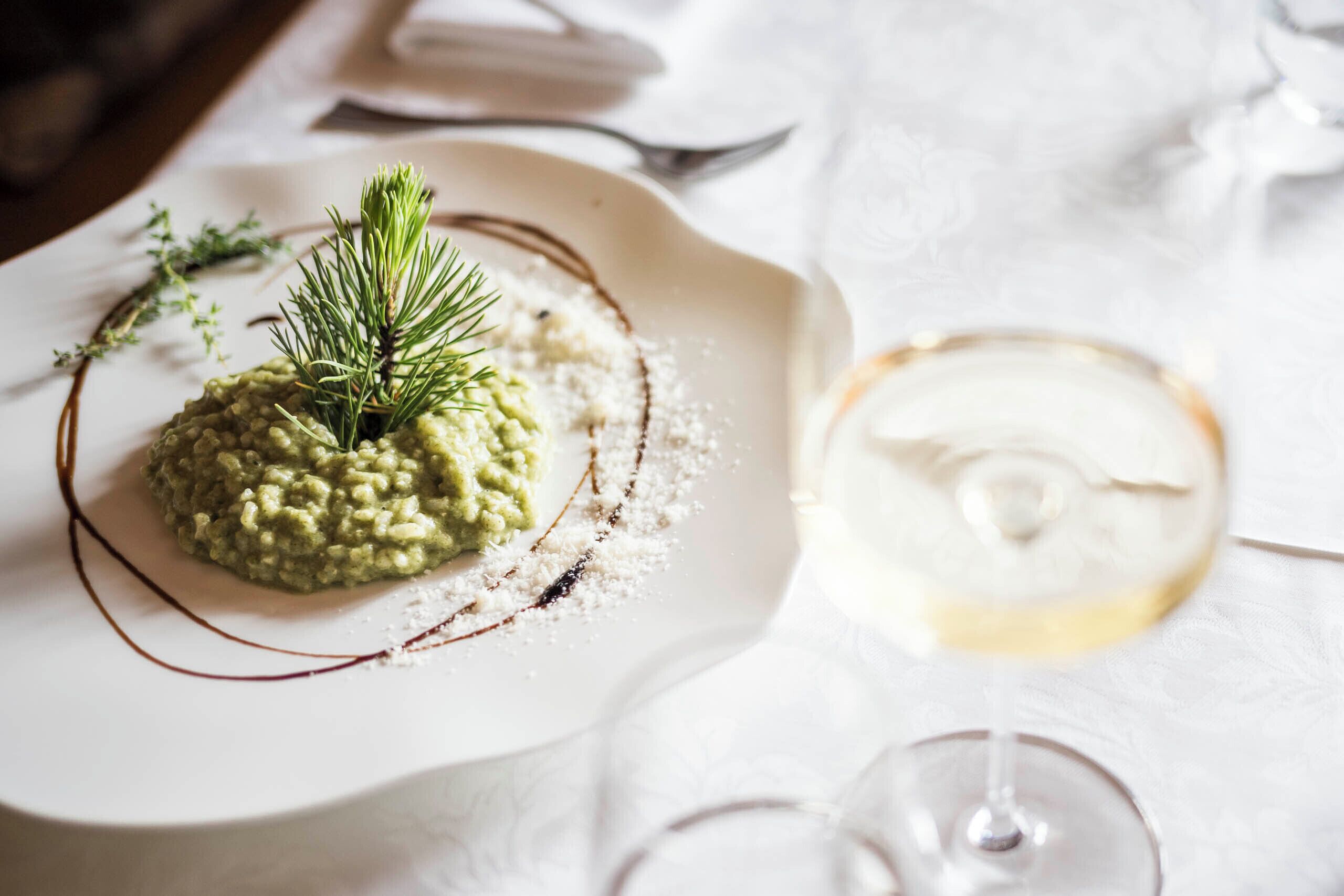 Een bord risotto, gegarneerd met kruiden, een glas witte wijn en een gevouwen servet op een tafel.