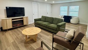 A modern living room with a flat-screen TV, a green sofa, a brown armchair, a round wooden coffee table, and a fireplace. - Lake Texoma Haven-Luxury Getaway Near Lake Texoma w/ Hot Tub (Pottsboro)