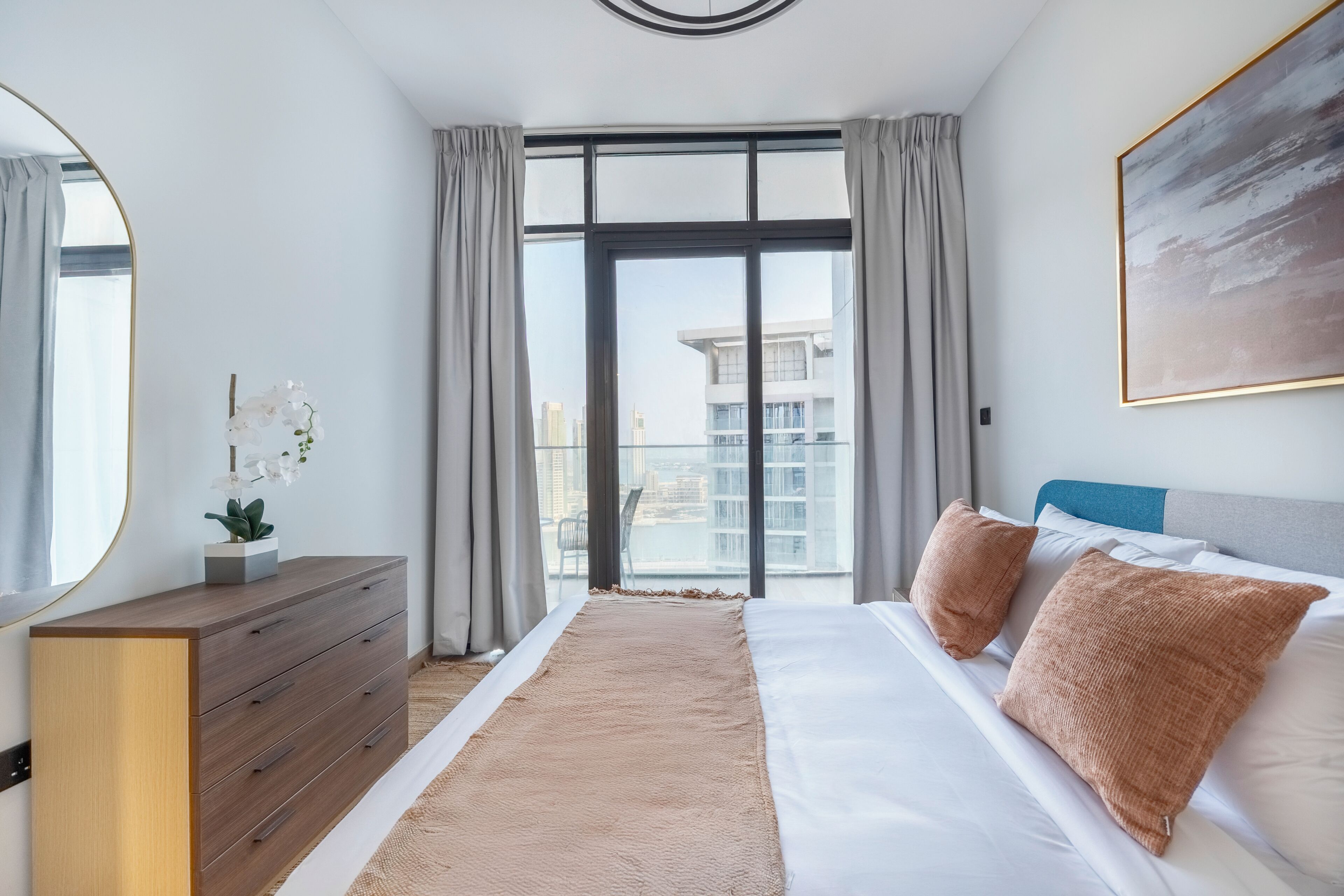 Un dormitorio moderno con una cama grande, un aparador, un espejo y vistas a la ciudad a través de la ventana.