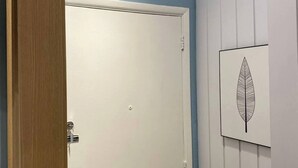 Puerta cerrada con ojo de cerradura y pomo, pared blanca con una obra de arte de hoja, y marco de madera.