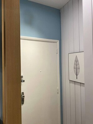 A closed door with a keyhole and a handle, a white wall with a leaf artwork, and a wooden door frame. - Adorável Studio Copacabana (Rio de Janeiro)