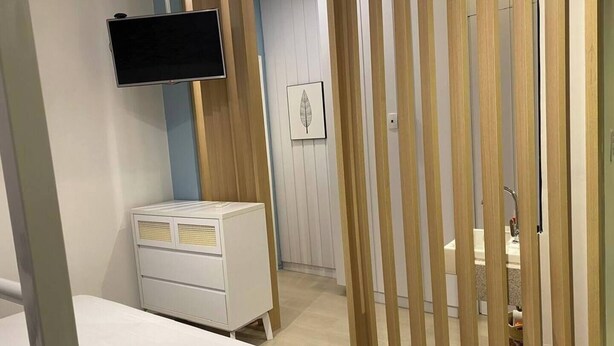 Un dormitorio con una cama, un televisor montado en la pared, un aparador y una partición de madera.
