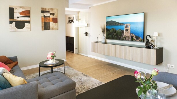 Ein Wohnzimmer mit Sofa, Couchtisch, Fernseher und einem Essbereich mit Tisch für zwei Personen.