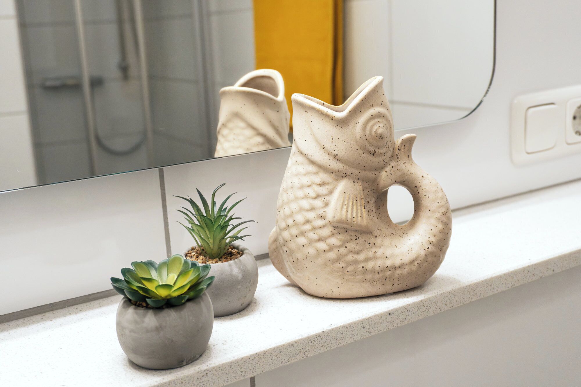 A bathroom with a white countertop, a mirror, and two ceramic fish-shaped vases with succulents.