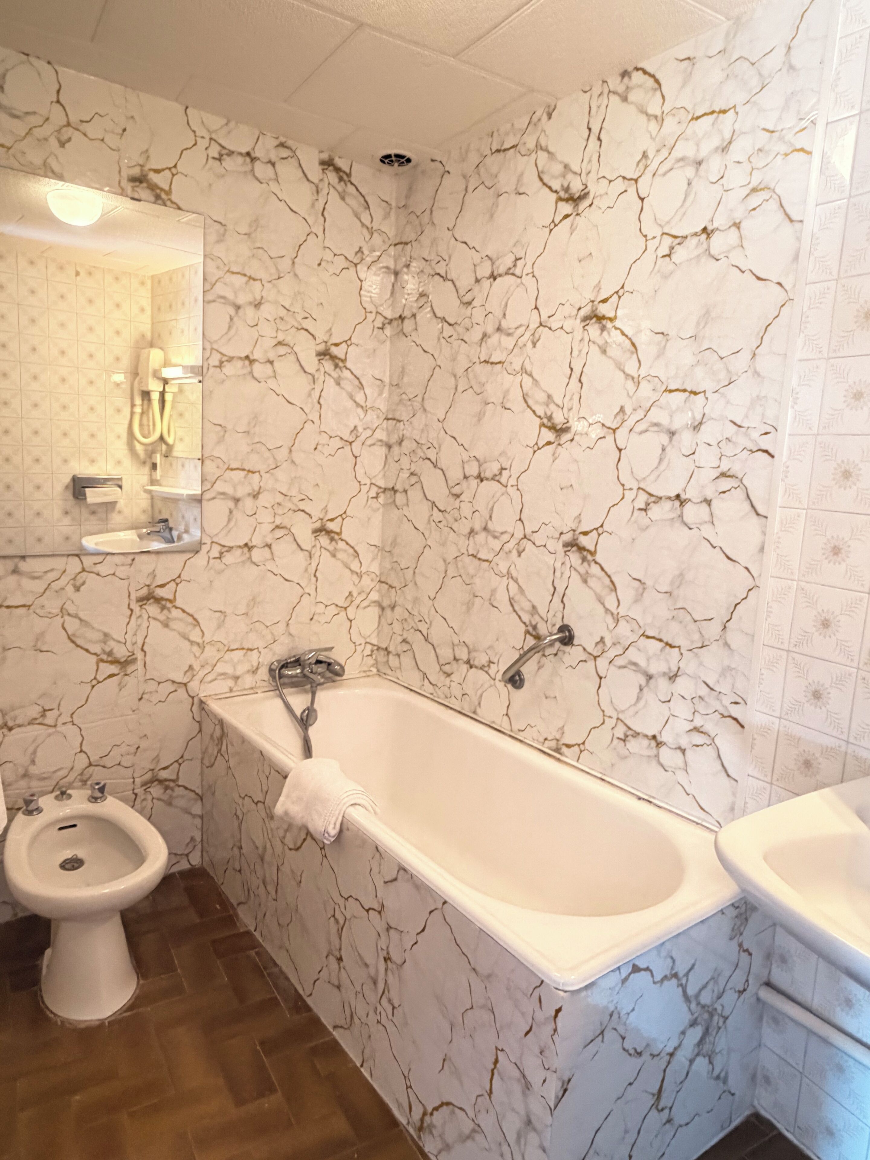 Un baño con pared de diseño de mármol, una bañera, un lavabo y un bidé.