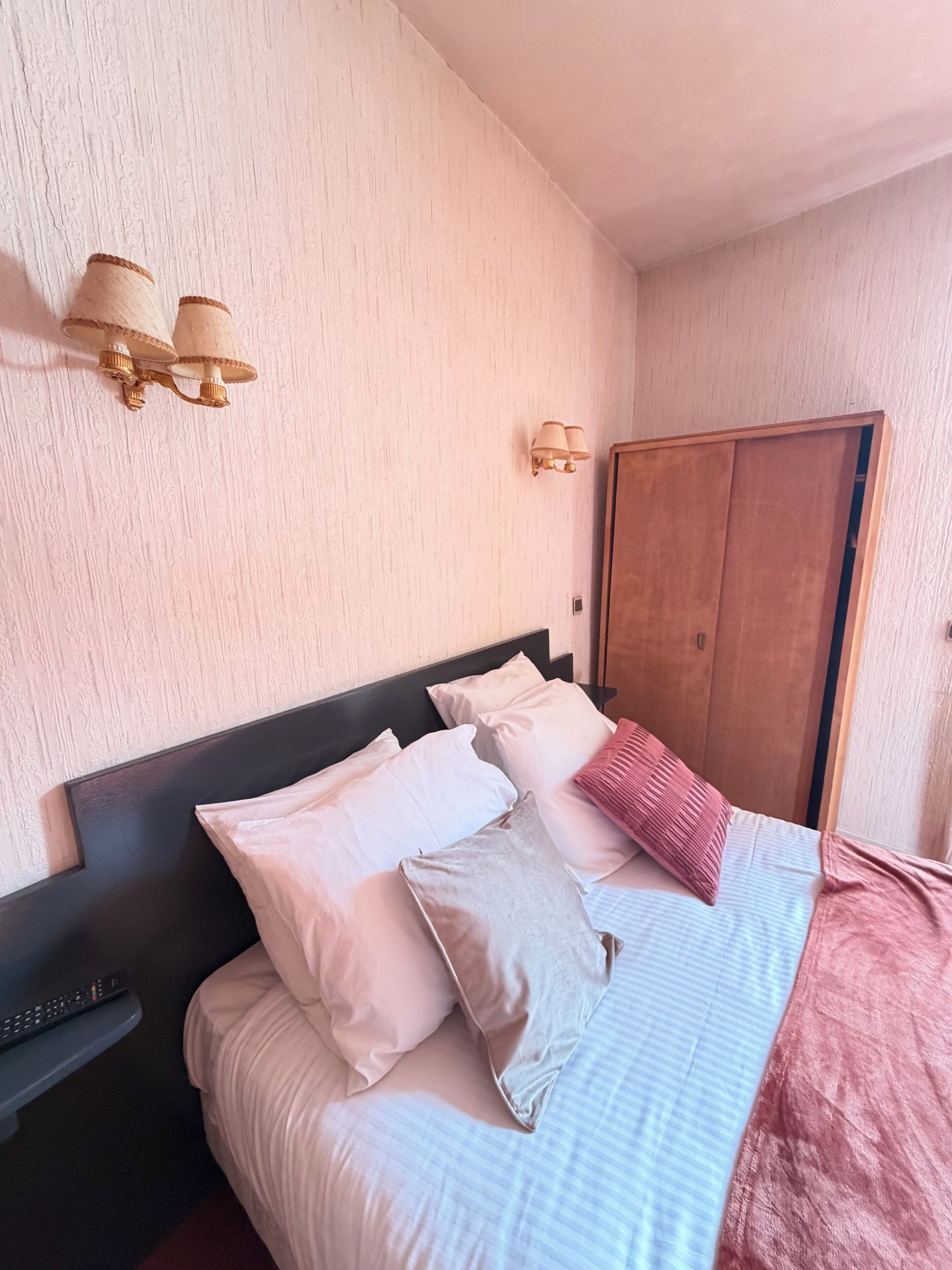 Un lit bien fait, avec des oreillers et une couverture, une table de chevet avec une télécommande et une armoire en bois.