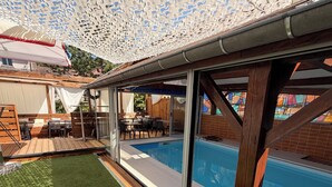A poolside area with a covered patio, a wooden deck, and a glass-enclosed pool. - HOTEL DE PARIS  (Poligny)