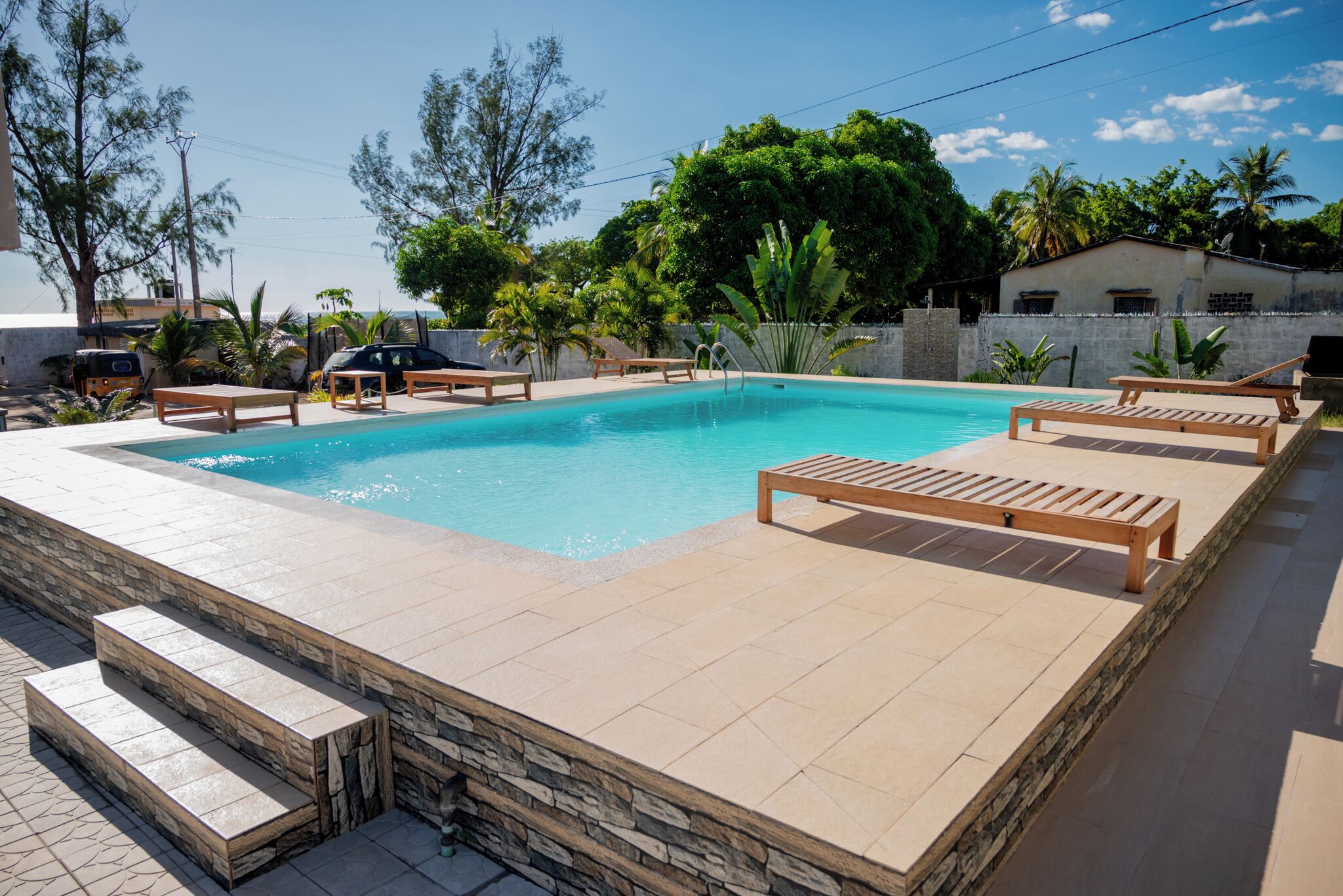 Uma piscina retangular com borda de pedra, rodeada por espreguiçadeiras e degraus de acesso.