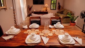 A dining area with a wooden table set for four, a television, a sofa, and a potted plant.