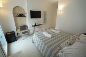 A hotel room with a bed, a desk, a chair, a TV, and a wardrobe. - Praialonga Suites with Pool and Garden (Isola di Capo Rizzuto)