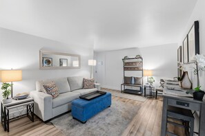 A modern living room with a sofa, ottoman, side table, lamp, bookshelf, and decorative plants. - Downtown Breckenridge Retreat at Edelweiss (Breckenridge)