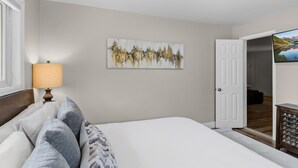 Um quarto com uma cama, um quadro, uma luminária e uma porta que dá para outro cômodo.