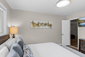 A bedroom with a bed, a painting, a lamp, and a door leading to another room. - Downtown Breckenridge Retreat at Edelweiss (Breckenridge)