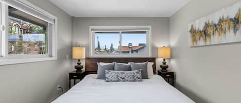 Une chambre avec un grand lit, deux tables de chevet avec des lampes, une fenêtre donnant sur un beau paysage et un tableau accroché au mur.