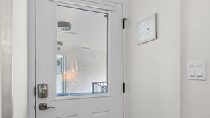 Uma porta branca com uma janela, um interruptor de luz fixado na parede e um documento emoldurado.