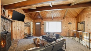 Ein rustikales Blockhaus-Interieur mit Kamin, einer Couch, einem Couchtisch und einem an der Wand befestigten Fernseher.