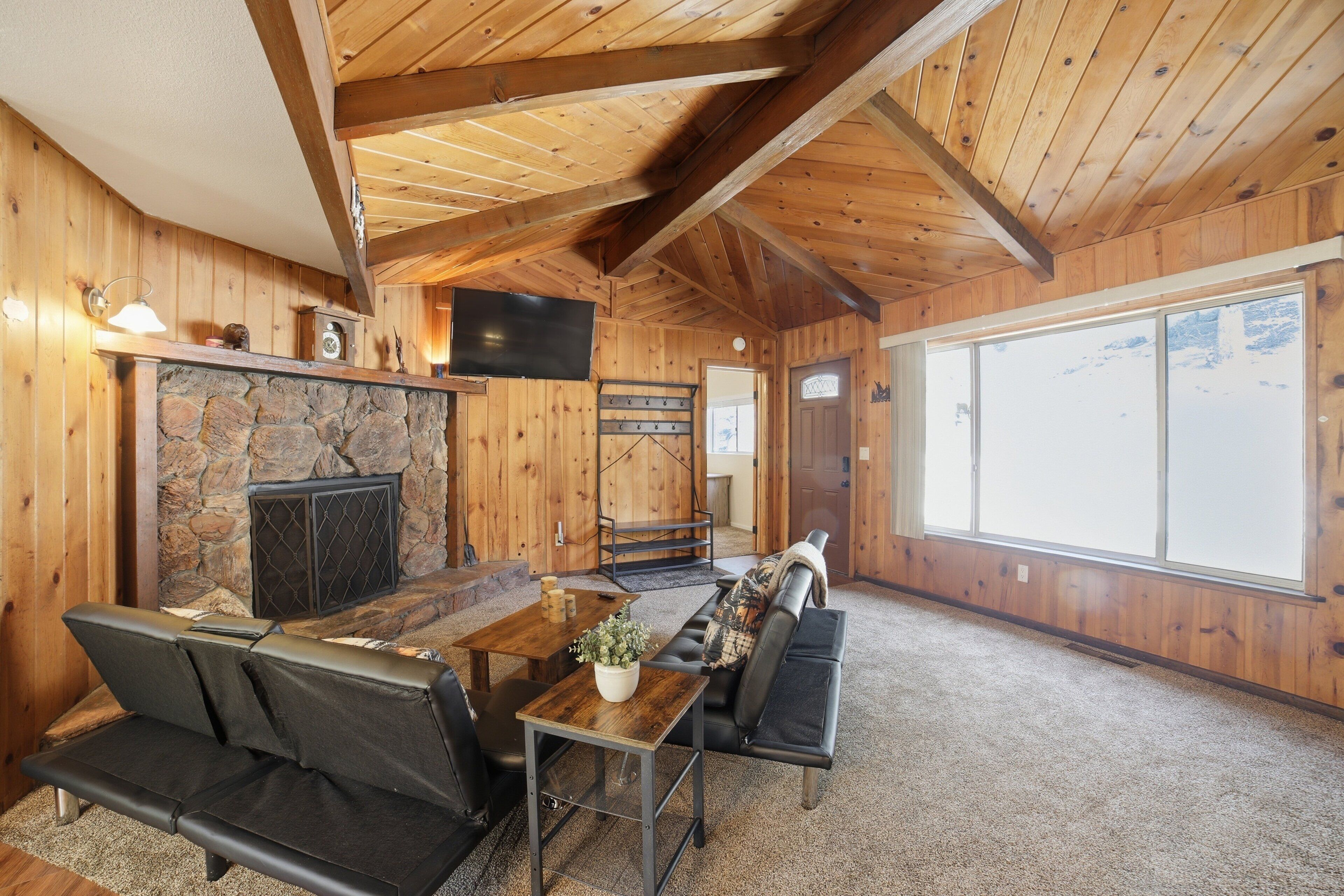 Un intérieur en bois avec une cheminée en pierre, un téléviseur et une grande fenêtre.