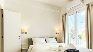 A hotel room with a bed, bedside lamps, a window with curtains, and a view of the outside. - Colorful Riviera Living in Voula Center (Voula)