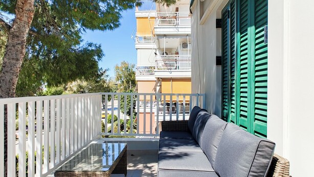 A balcony with a wicker table, a sofa, and a white railing. - Colorful Riviera Living in Voula Center (Voula)