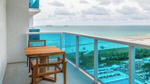 Een balkon met een houten tafel en stoelen, met uitzicht op een zwembad en een strand.