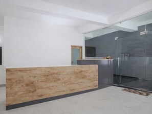 A modern reception area with a wooden counter, a glass partition, and a door leading to another room. - Hotel O Sundarpur Crossway Varanasi (Varanasi)