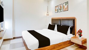 A modern hotel room with a large bed, a bedside table with a vase of flowers, and a wall-mounted TV. - Saver Double Ssm Murugan Rooms (Sriperumbudur)
