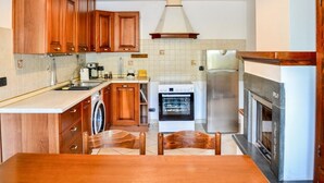 A kitchen with wooden cabinets, a washing machine, a stove, a refrigerator, and a dining table with chairs. - Casa Marina - Minucciano (Minucciano)