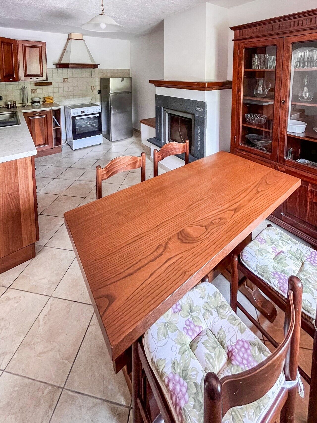Una cucina con un tavolo di legno, sedie e un pensile con vetri.