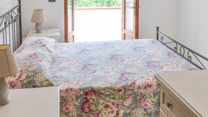 Un dormitorio con cama, mesita de noche, cómoda, ventana y puerta abierta que da a un balcón.