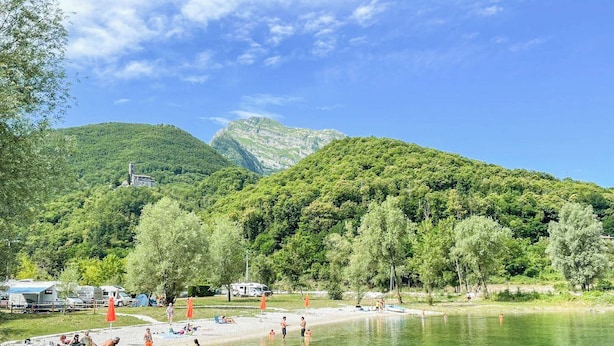Camping junto al lago con vehículos recreativos, un barco y gente cerca del agua.