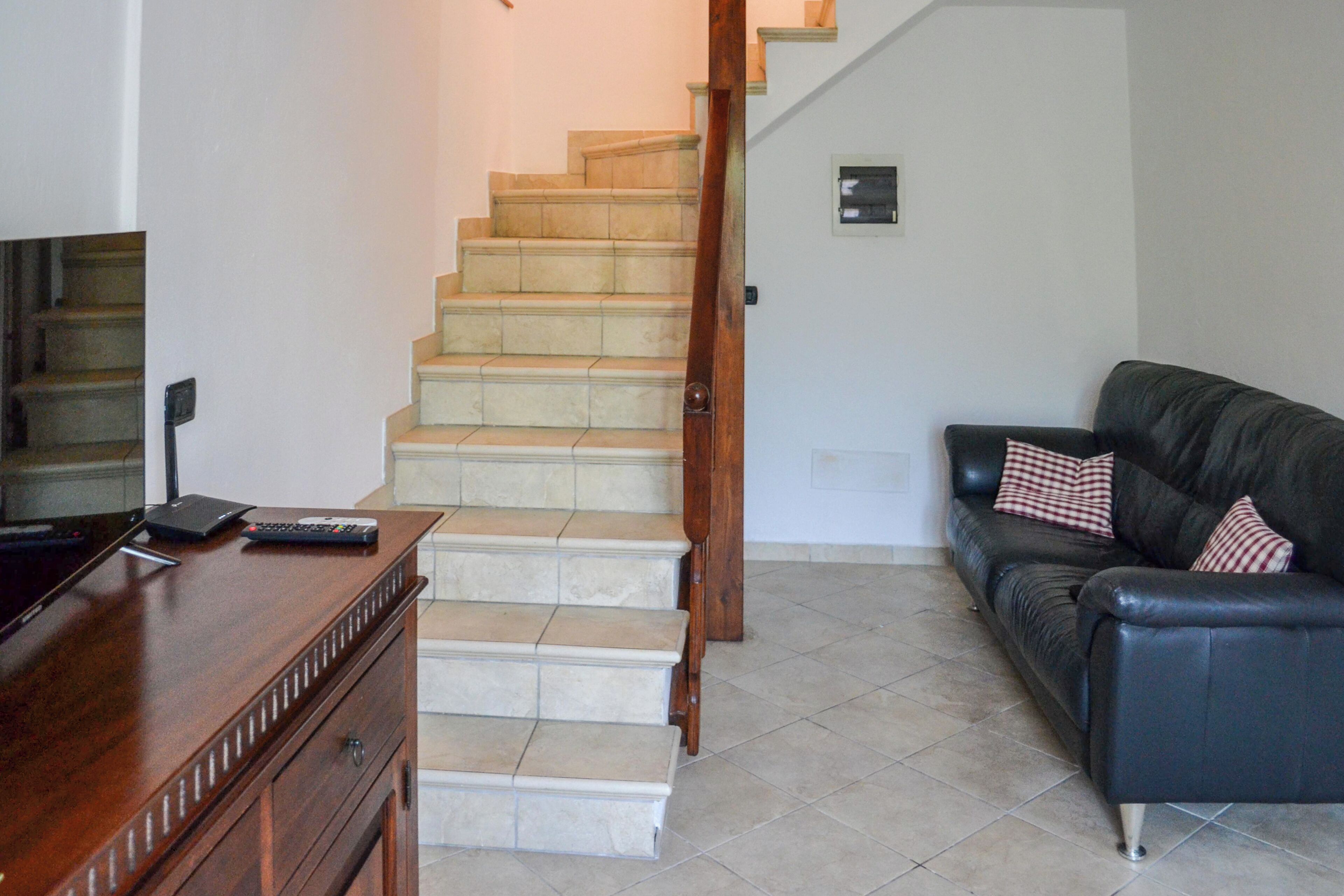 A staircase leading to a landing, a dark leather sofa with patterned cushions, and a wooden dresser with a remote control on top.