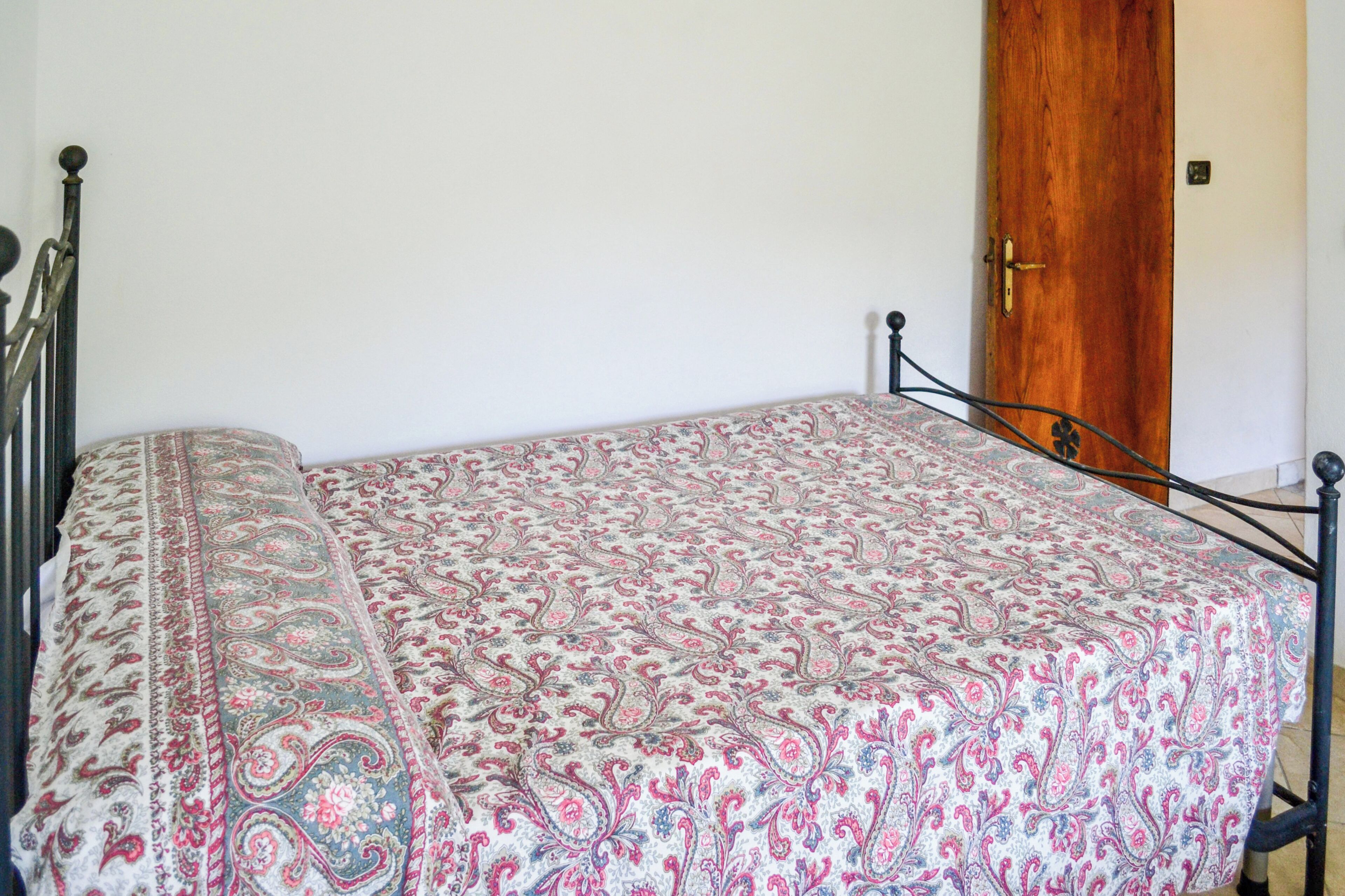 A bed with a patterned bedspread, a wooden door, and a metal bed frame.