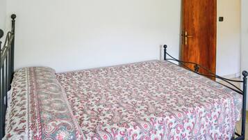 A bed with a patterned bedspread, a wooden door, and a metal bed frame.