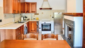 Una cocina con armarios de madera, lavadora, horno, refrigerador y una mesa de comedor con sillas.