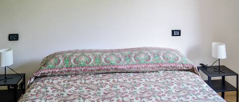 A bed with a patterned bedspread, two bedside tables with lamps, and wall-mounted switches.