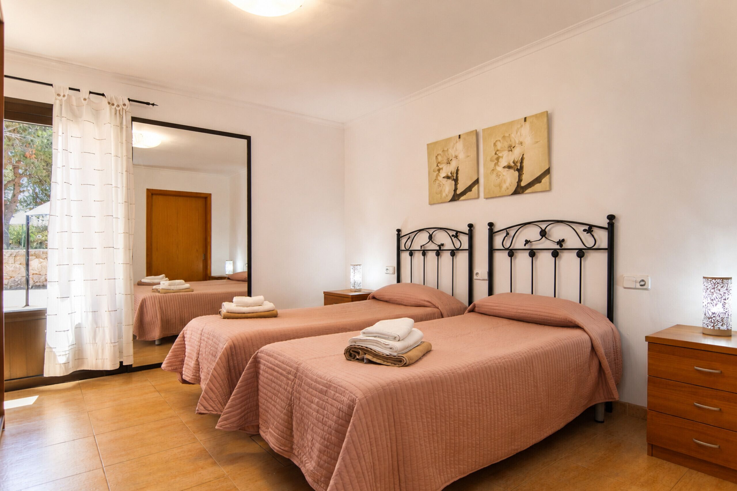 A hotel room with two beds, a wooden dresser, a mirror, and artwork on the wall.