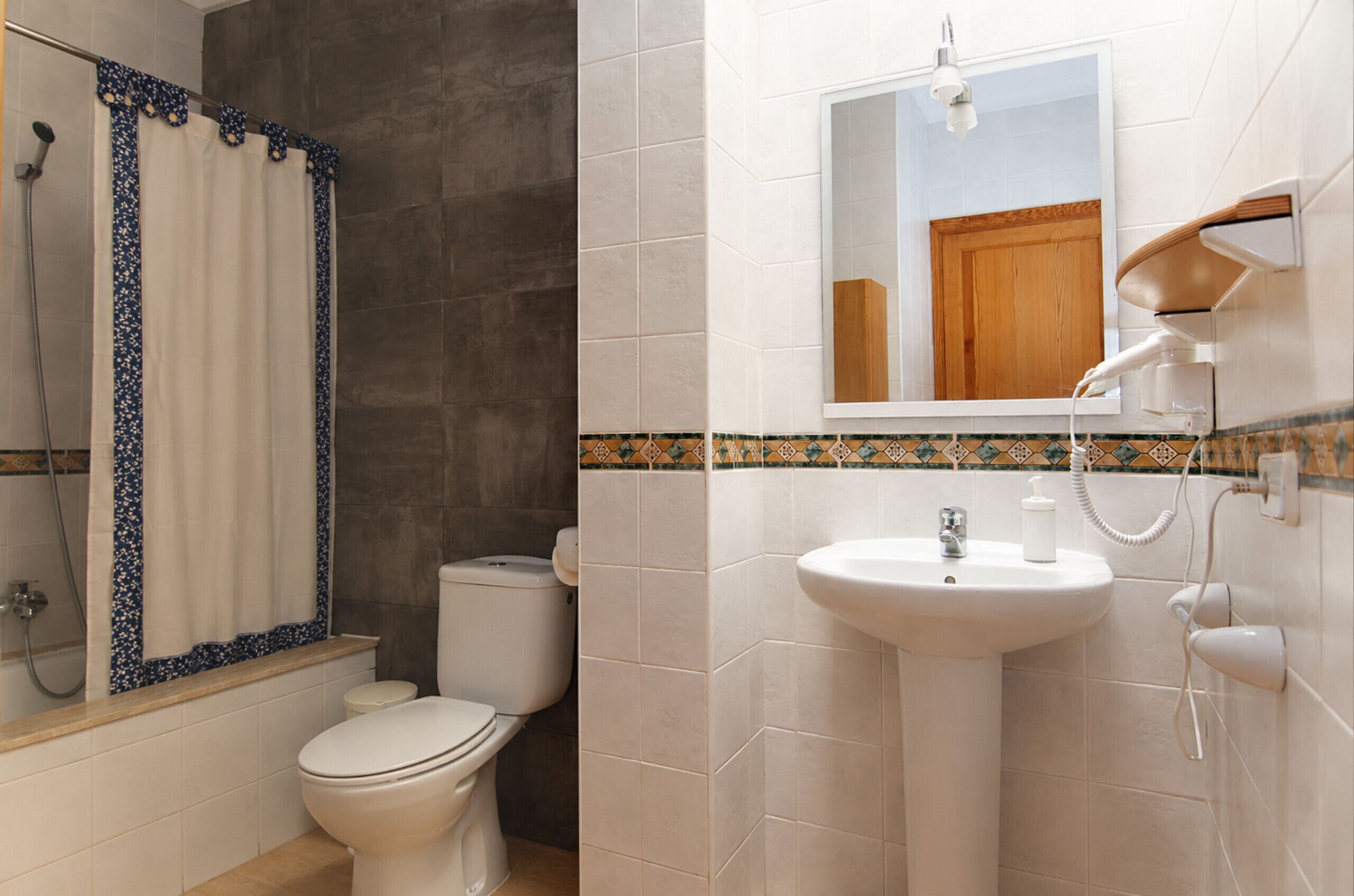 A bathroom with a shower, toilet, sink, and mirror.
