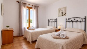 A room with two beds, a wooden cabinet, a window with curtains, and a wall-mounted picture. - 286 Palmitos 1 by Mallorca Charme (Can Picafort)