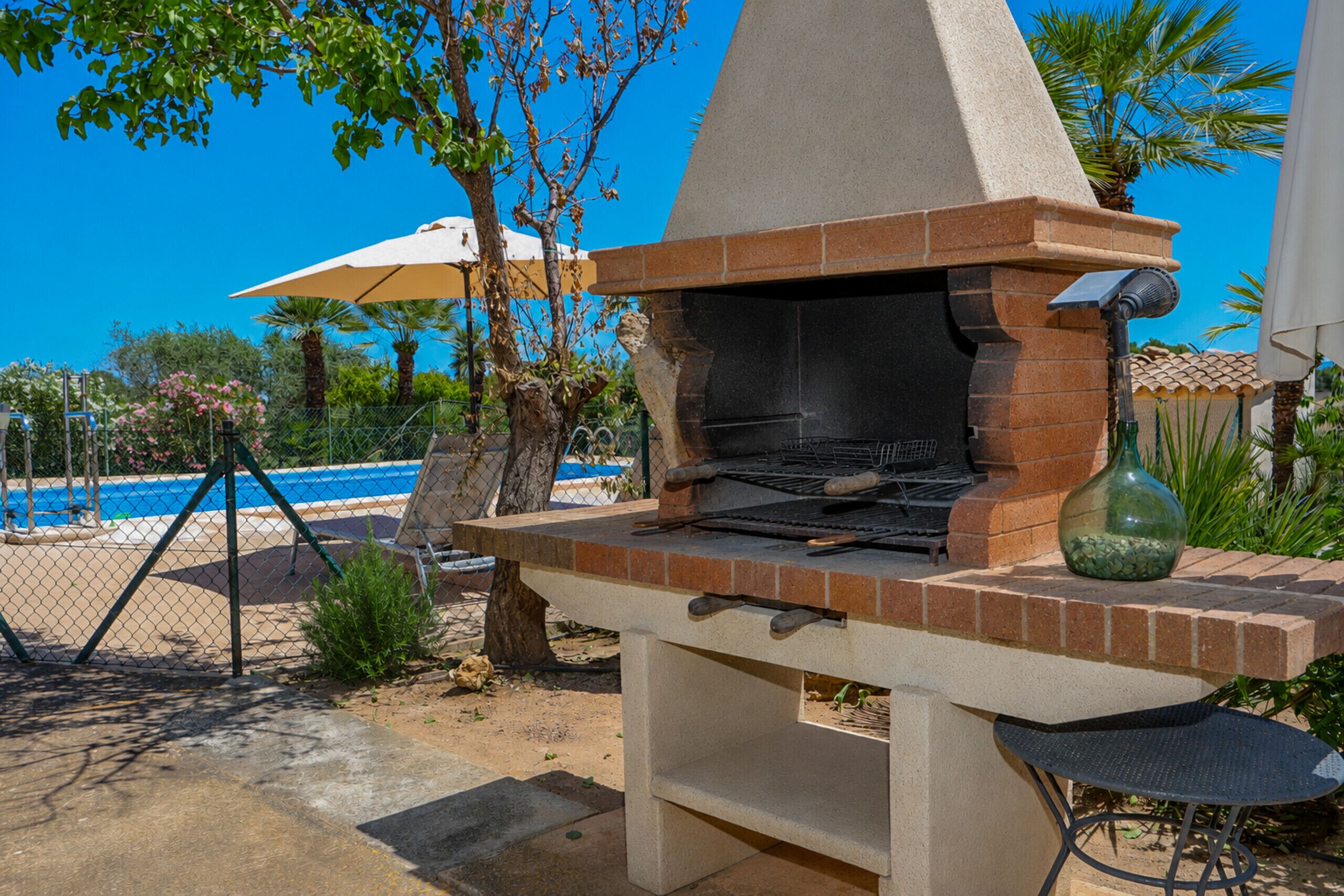 An outdoor brick barbecue grill with a chimney, a table, and a chair.