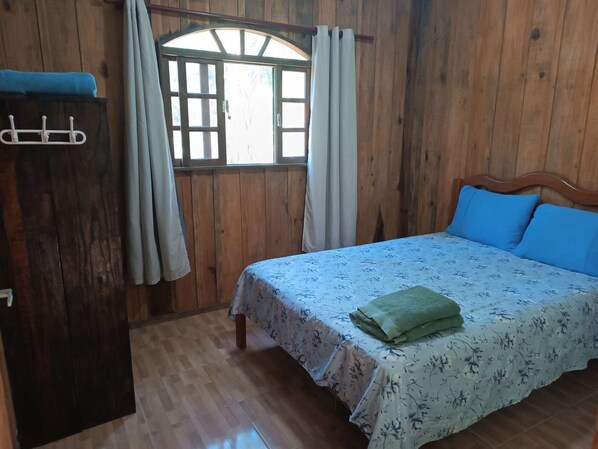 Une pièce en bois avec un lit, une armoire en bois et une fenêtre avec des rideaux.
